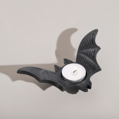 Bat-shaped tealight candle holder with white candle and wick, matte black finish.