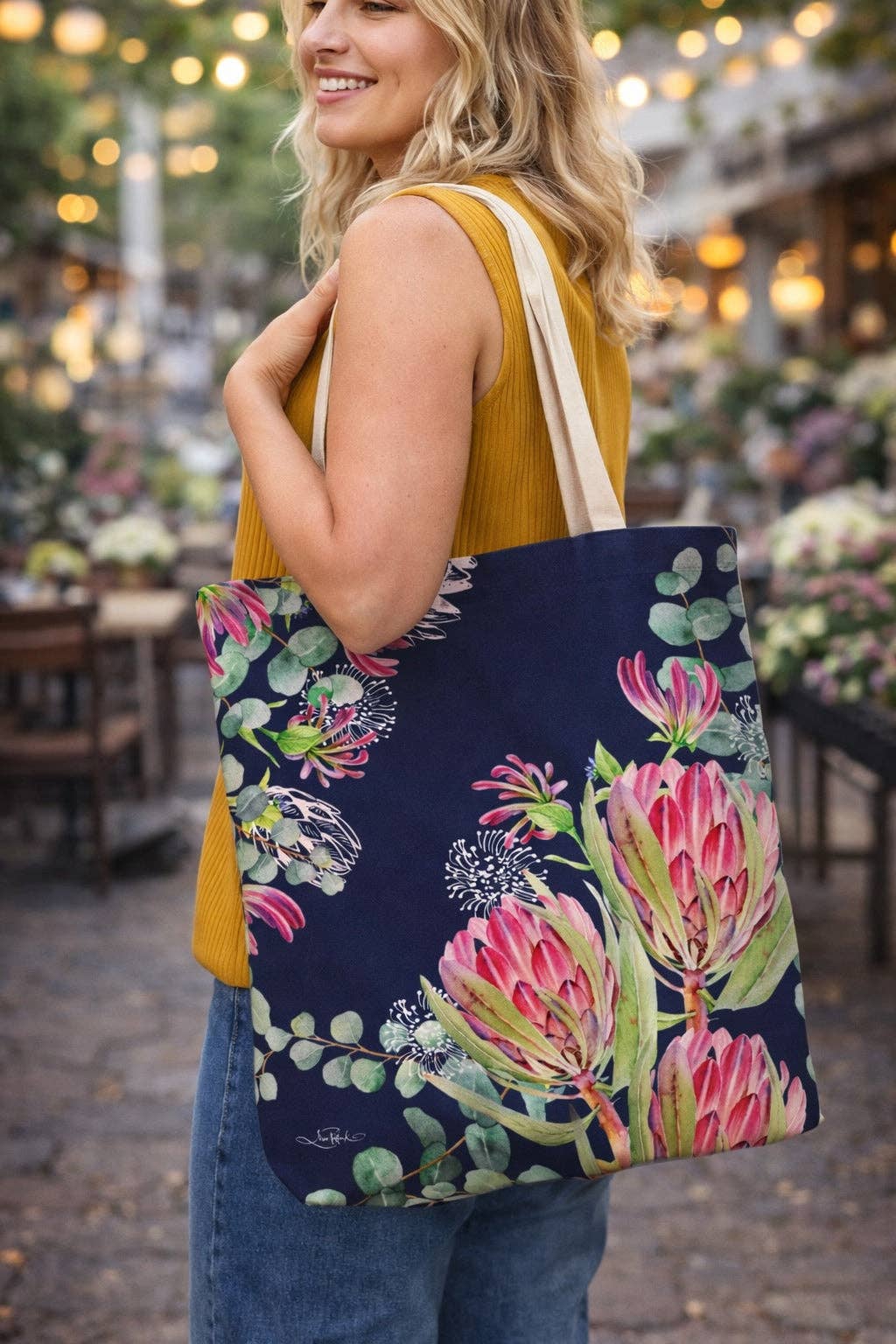 Navy floral tote bag with pink protea-style blooms and green leaves, carried by strap