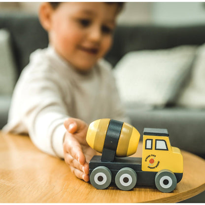 Toy cement mixer truck with yellow cab, black drum, and gray wheels in child’s hand