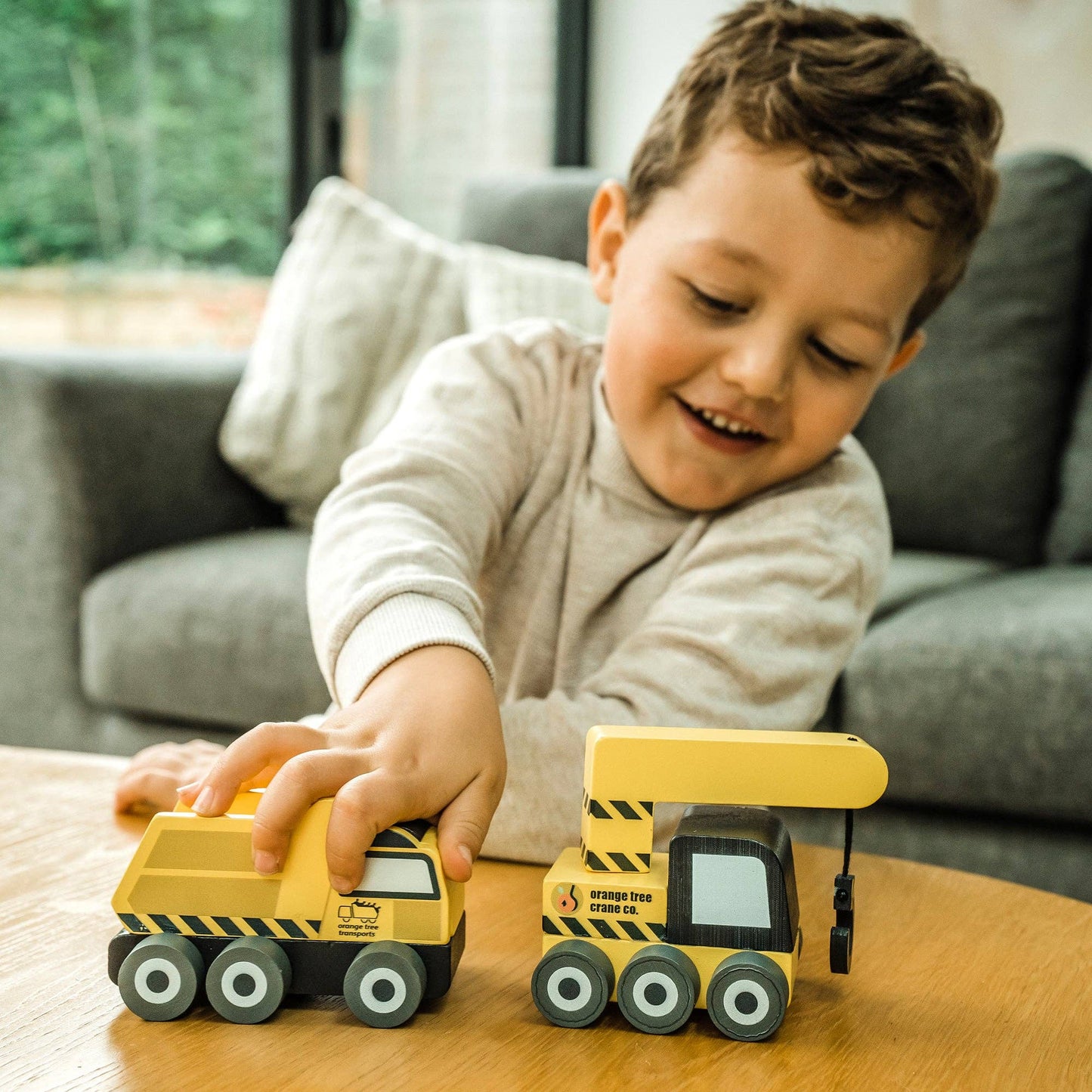 Two yellow construction truck toys on table with a child smiling nearby