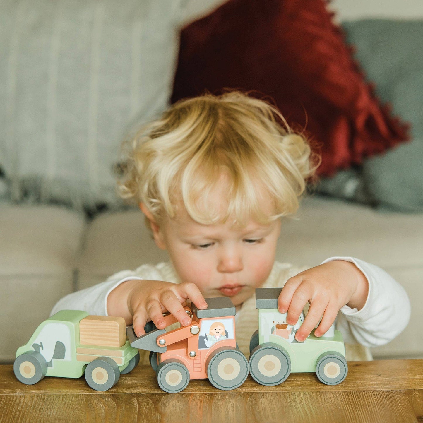 Green wooden tractor toy with gray wheels; child plays with it on a table