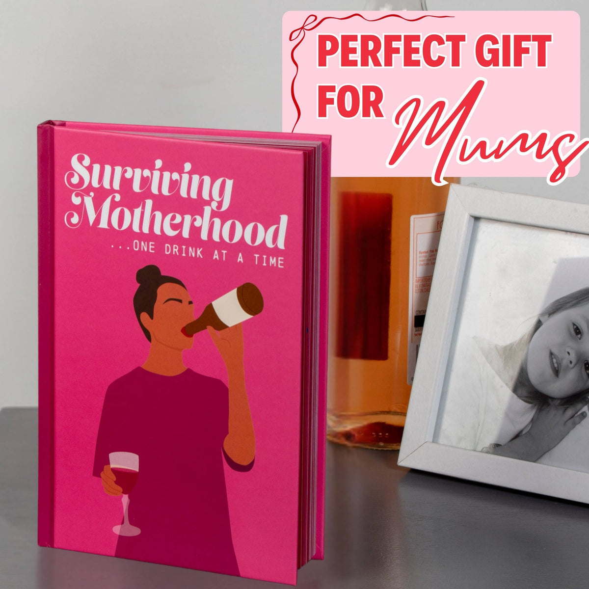 Surviving Motherhood gift book with pink cover next to a gray portrait photo frame