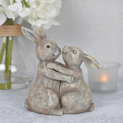 Beige bunny rabbit ornament pair hugging, close view on textured resin surfaces