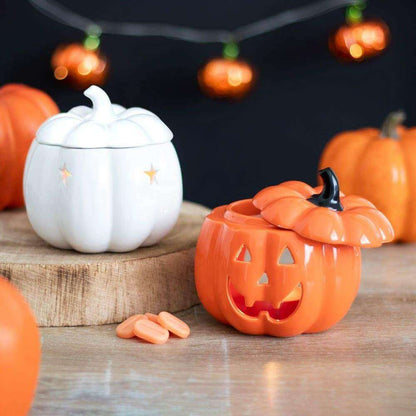 White ceramic pumpkin oil burner with star details, with orange jack-o’-lantern beside it